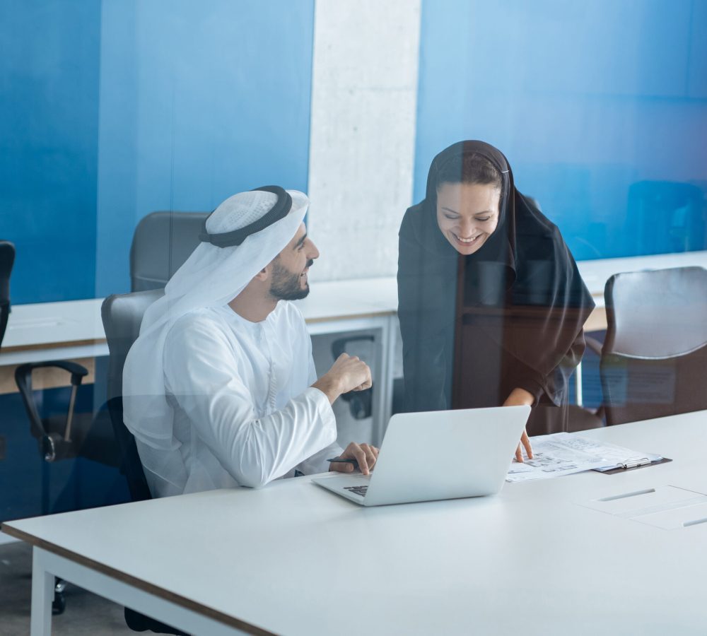 Man and woman with traditional clothes working in a business office of Dubai. Portraits of  successful entrepreneurs businessman and businesswoman in formal emirates outfits. Concept about middle eastern cultures, lifestyle and professional occupations